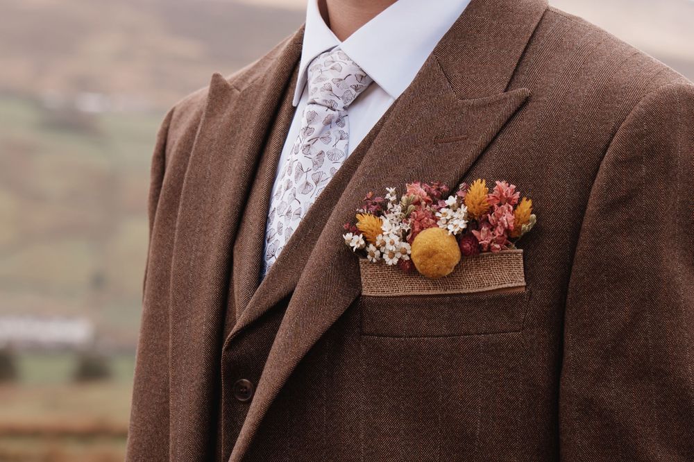 Groom in brown tweed suit with colorful dried flower boutonniere in pocket.