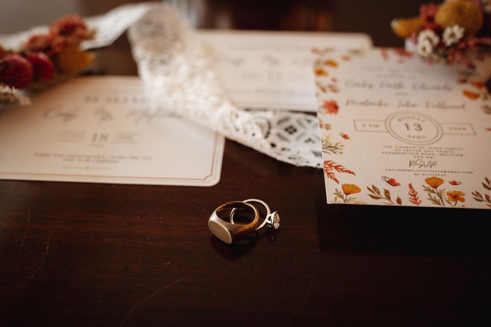 Wedding rings and stationery with autumn floral design displayed on dark wooden surface.