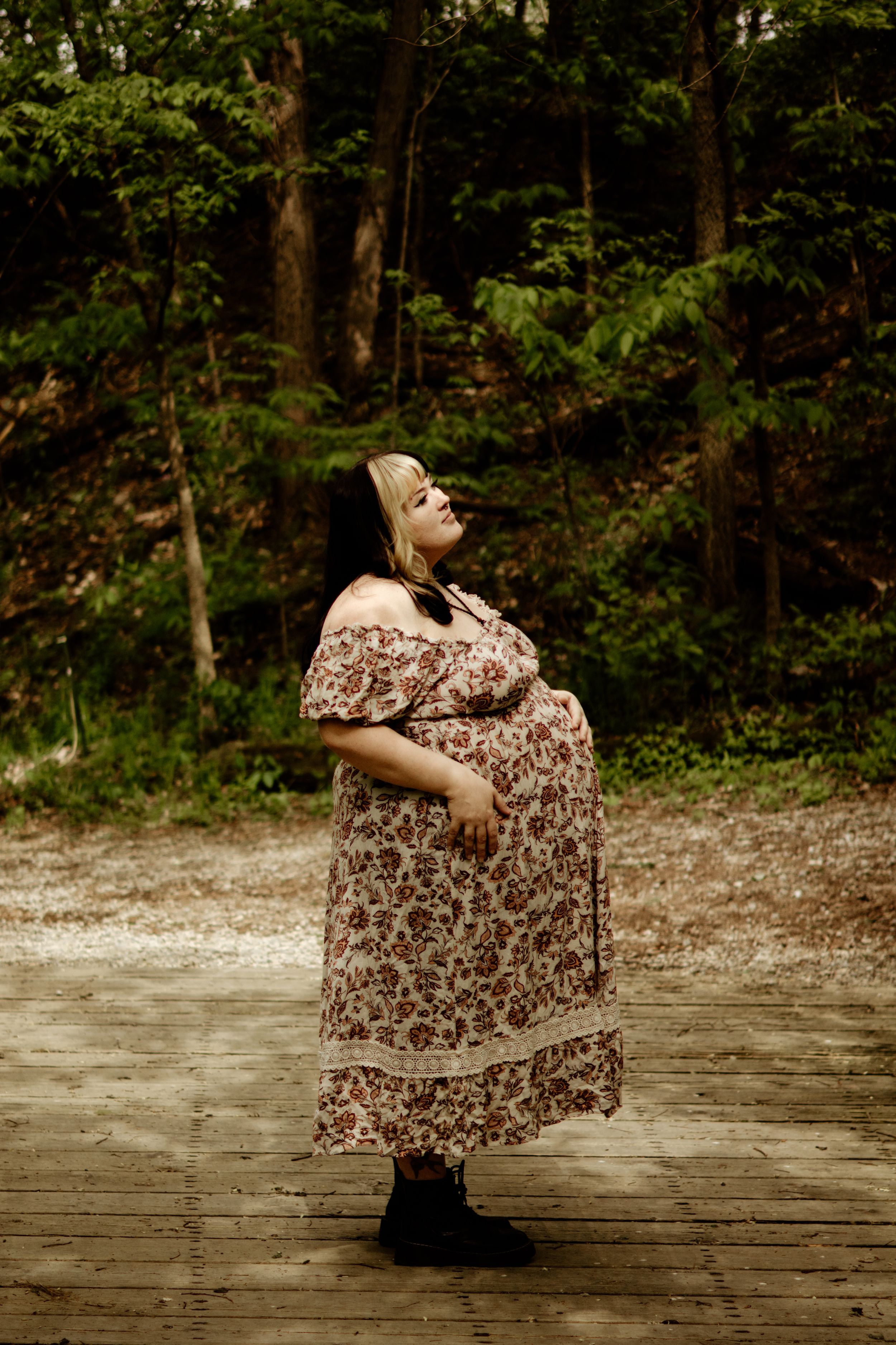 An expecting mom standing in woods. Sunlight giving her a nice warm glow.