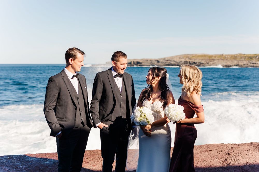 Wedding party laughs together while walking along a scenic beach with waves crashing in the background.