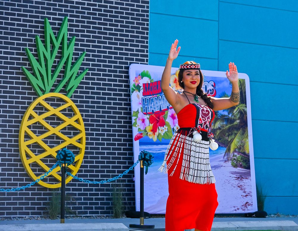 A woman in traditional red Polynesian costume dances beside a decorative pineapple at Hawaiian Bros restaurant.