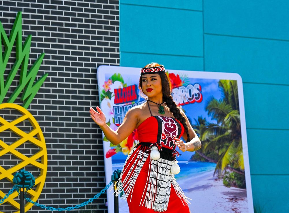 A woman in a red traditional Polynesian outfit dances gracefully outside Hawaiian Bros restaurant.