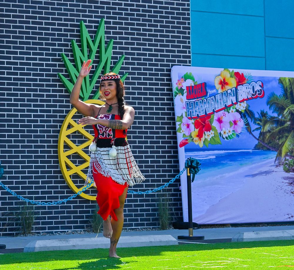 Female dancer in traditional red and white Polynesian costume performs beside pineapple decor at Hawaiian Bros.