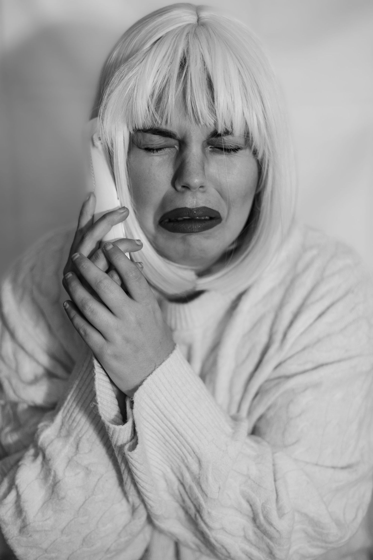 A series of black and white portraits showing emotional expressions and hand gestures while wearing a white sweater.