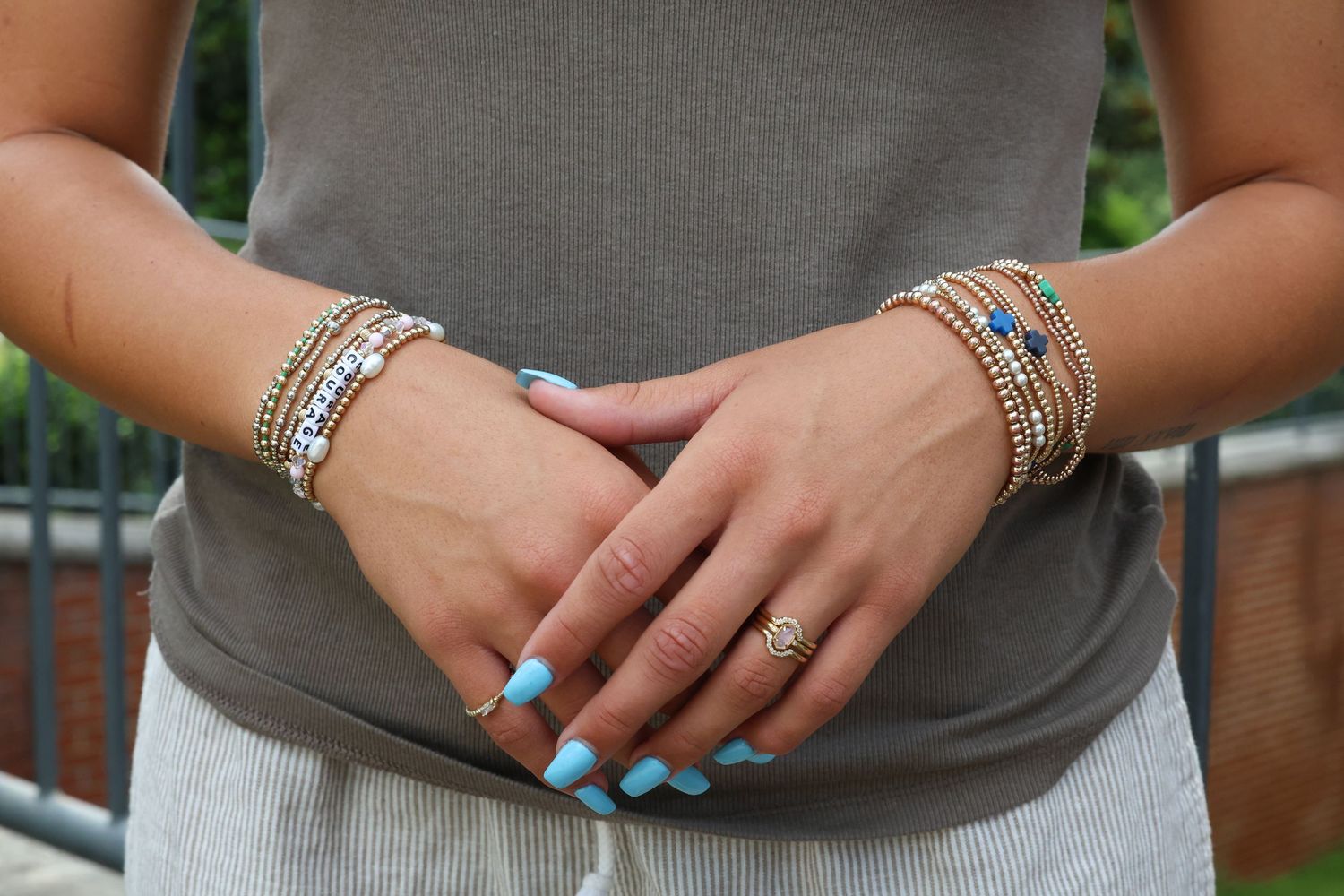 Close-up view of hands wearing multiple silver and turquoise stacked rings and bracelets against a gray shirt.