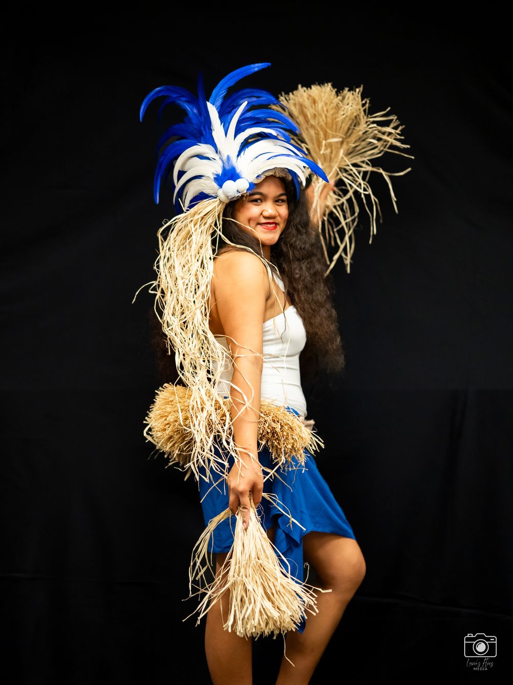 A dancer in a blue hat and white costume performs dynamic movements against a black background during a dance routine.