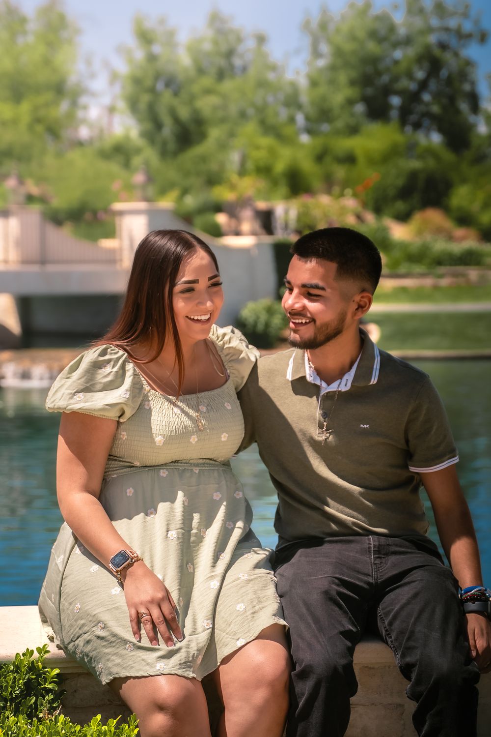 A couple sits together by a lake, sharing joyful laughter in casual attire.