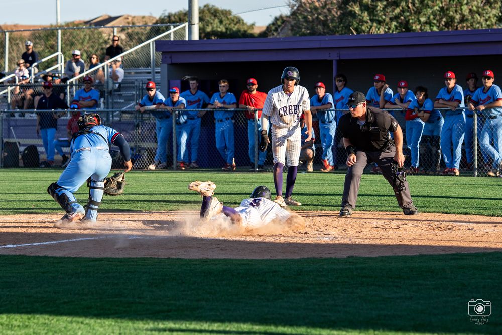 Baseball player slides into home plate during game while catcher prepares to make the tag as umpire watches closely.