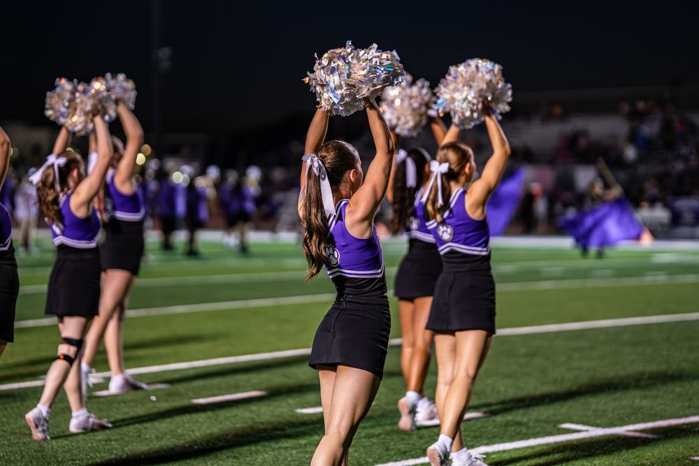 Cheerleaders perform routines on the field during a nighttime sports event.
