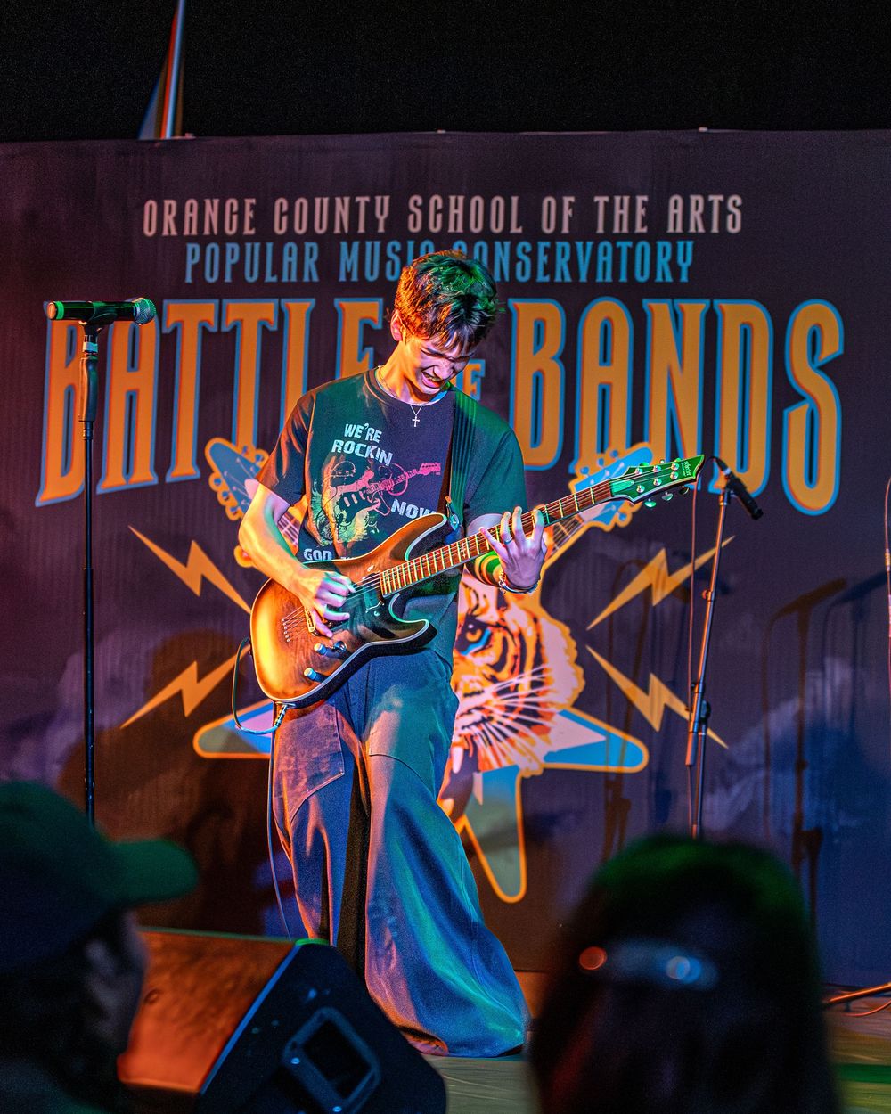 Guitarist performs on stage with colorful blue and orange lighting at Orange County School of the Arts concert.