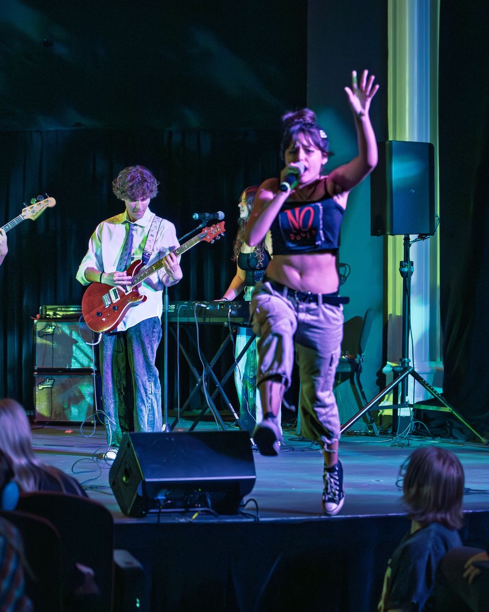 Musicians perform on stage in a dimly lit venue with purple and blue lighting effects creating a moody atmosphere.
