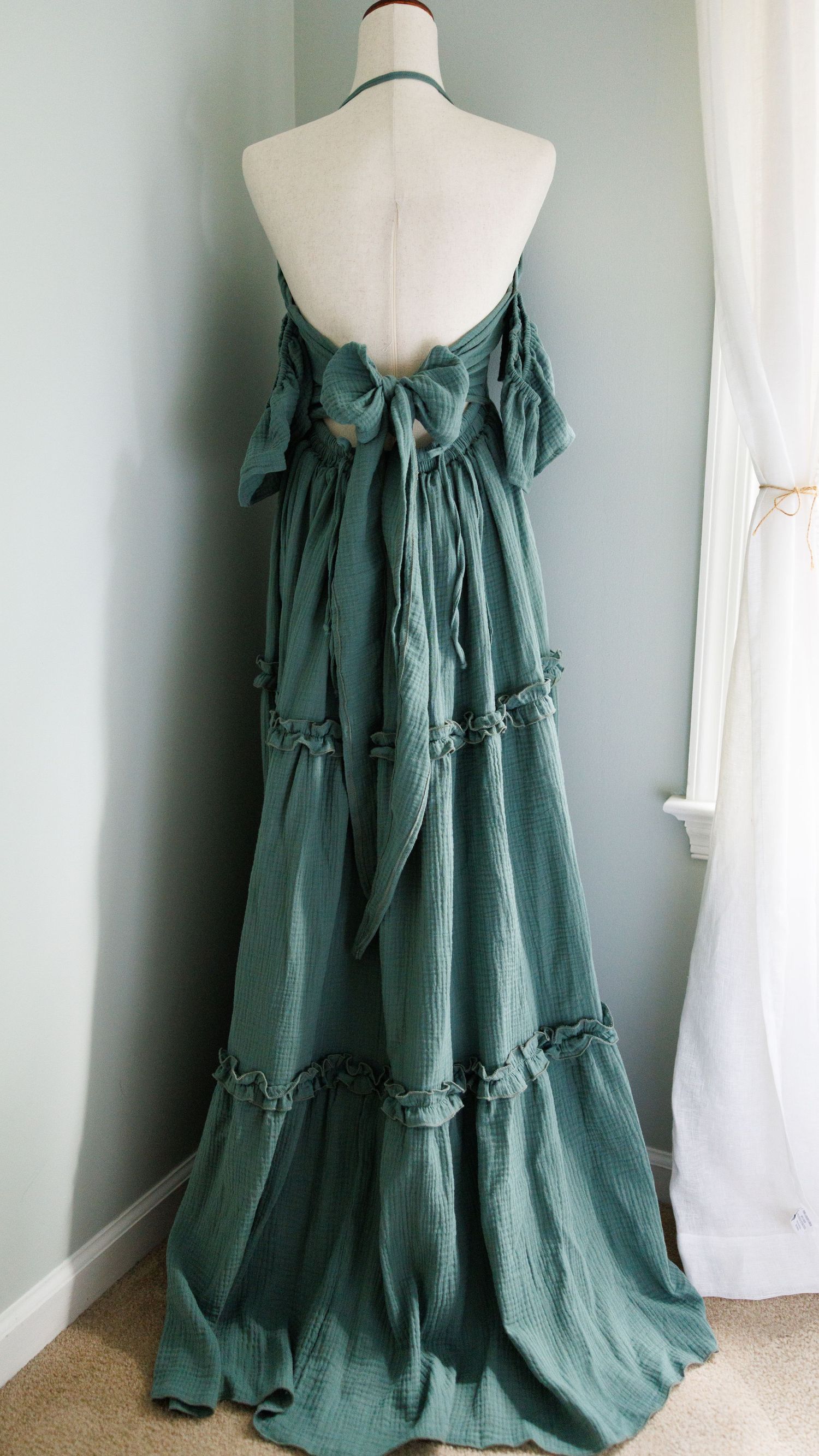 Green tiered cotton dress with ruffles and bow detail displayed on mannequin form against light wall.
