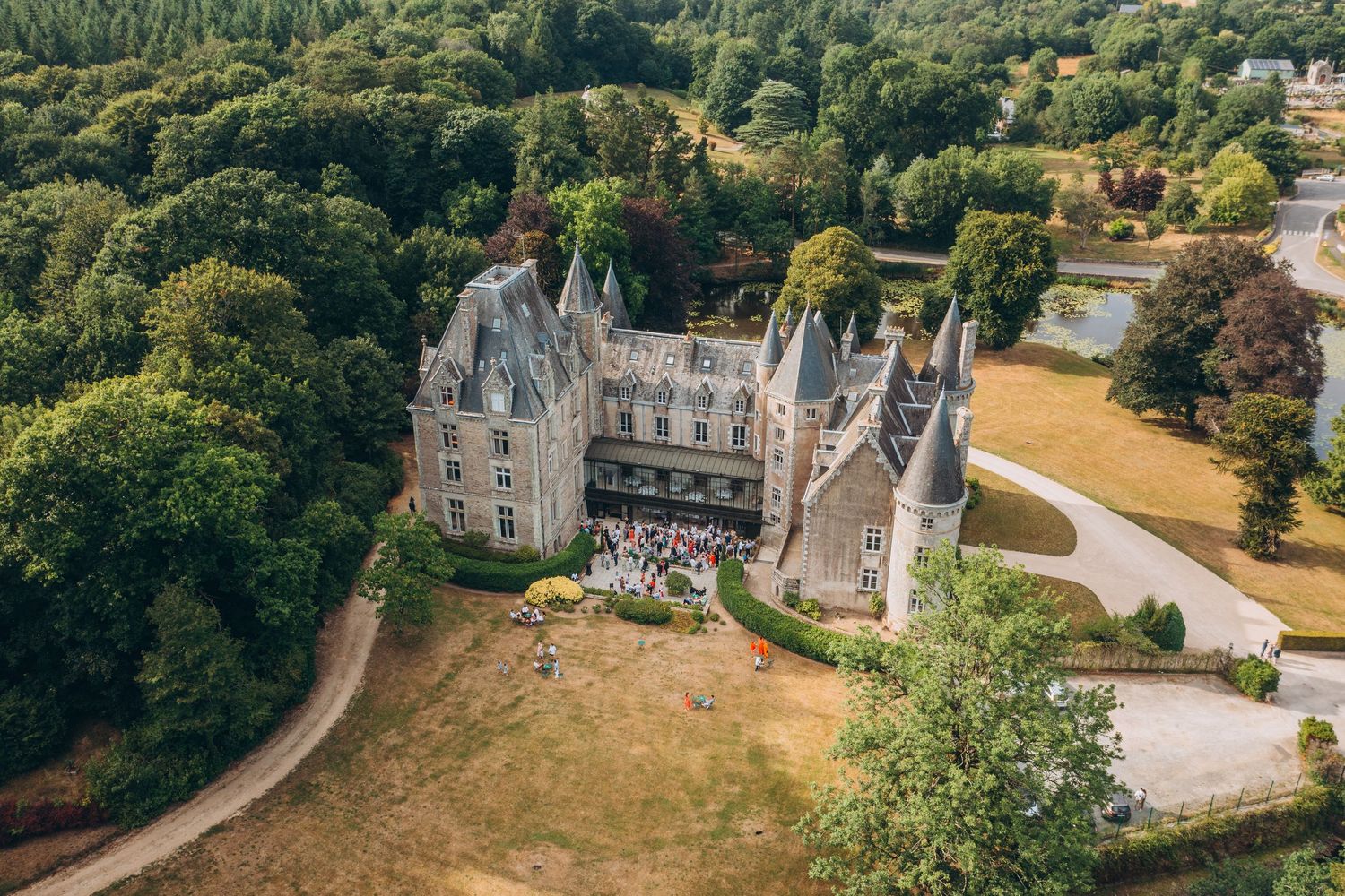 Aerial view of a historic French chateau with manicured gardens and winding pathways surrounded by lush forest.