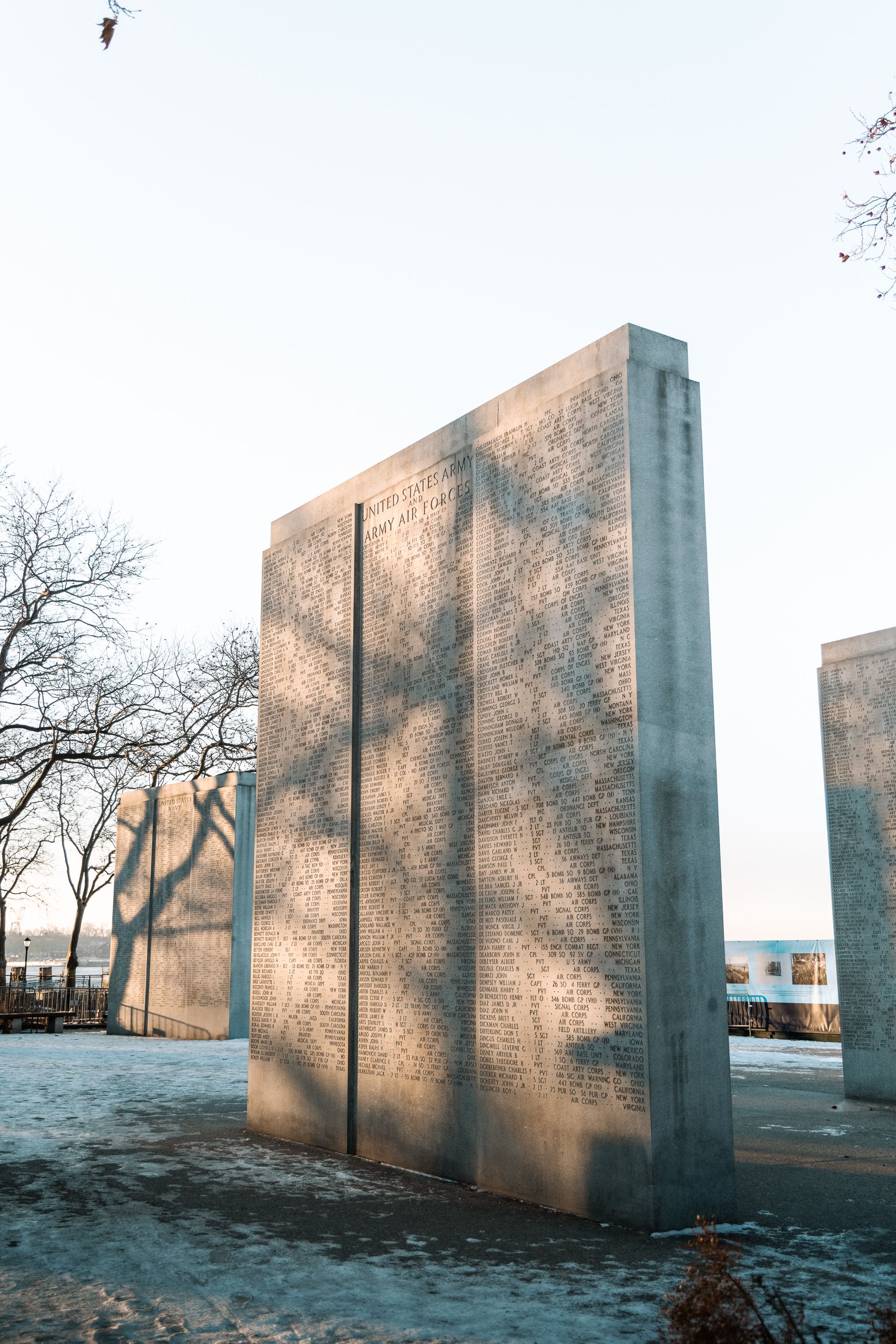 Concrete memorial wall casting shadows in winter sunlight with snow on ground.