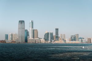 Wide panoramic view of Lower Manhattan's skyline across the harbor on a sunny day.