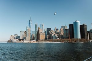 Panoramic view of the Manhattan skyline from New York Harbor with skyscrapers reflecting in the water.
