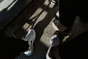 Shadow patterns of pedestrians walking on cobblestone pavement in dramatic lighting.