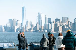 Tourists viewing the Manhattan skyline from an observation deck on a clear day.