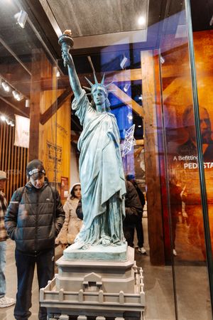 Scale model of Statue of Liberty displayed in museum exhibit with visitors viewing.