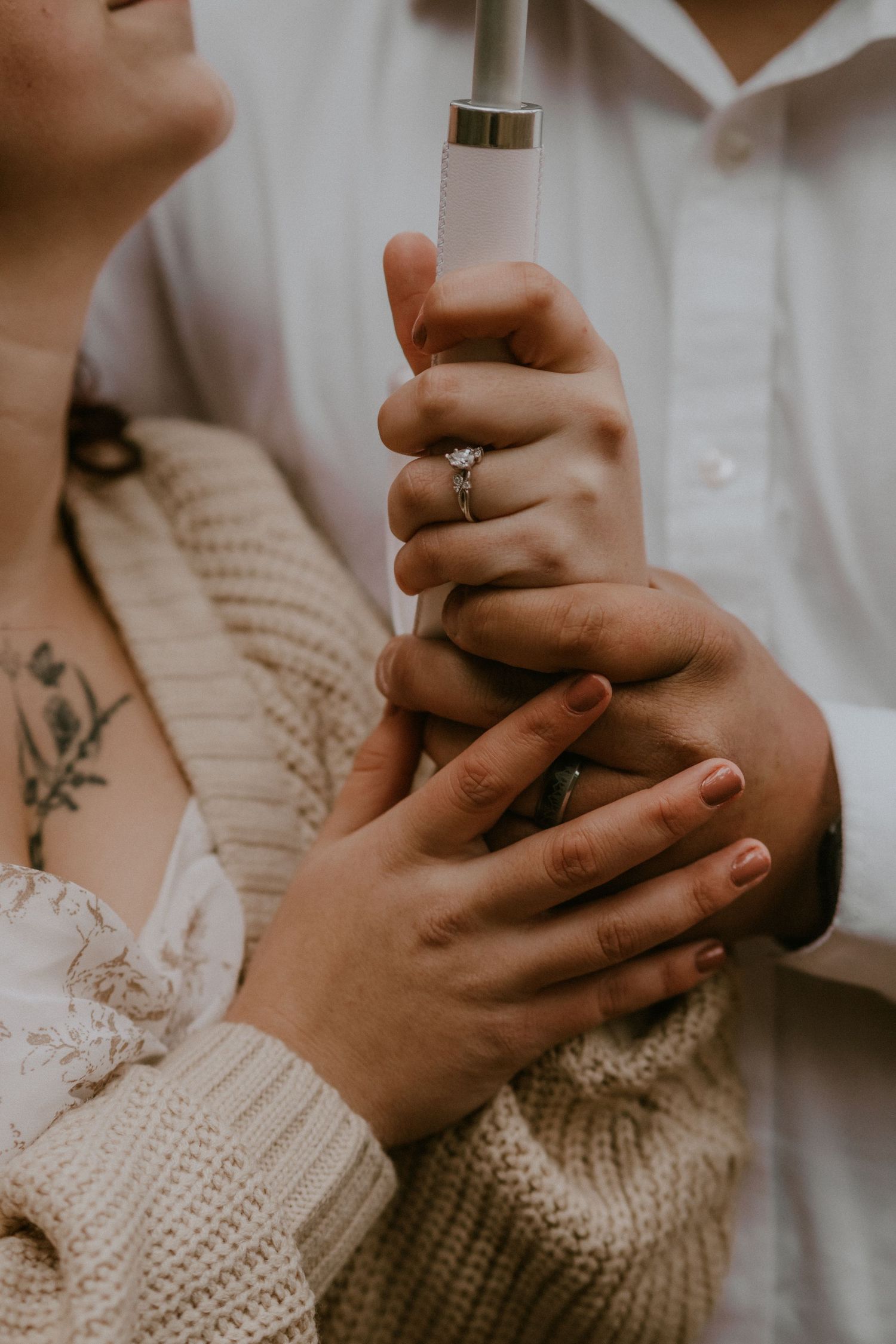 Close-up view of hands holding each other tenderly while wearing a white shirt and knit sweater.