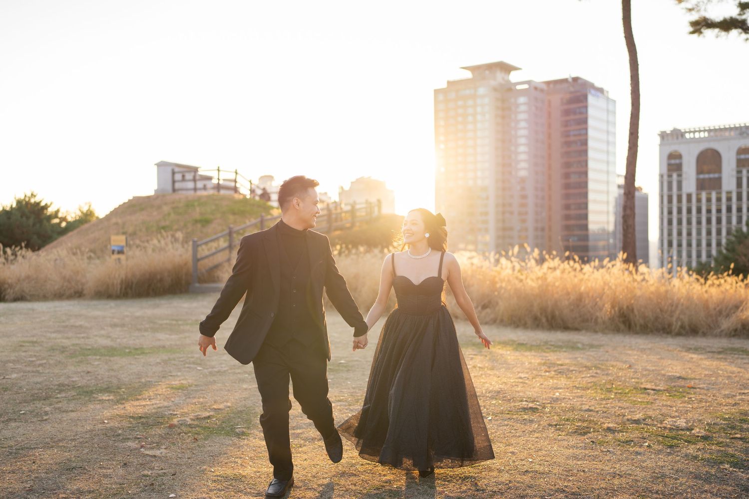 Couple walking hand in hand through a golden field during sunset with lens flare creating a romantic silhouette.