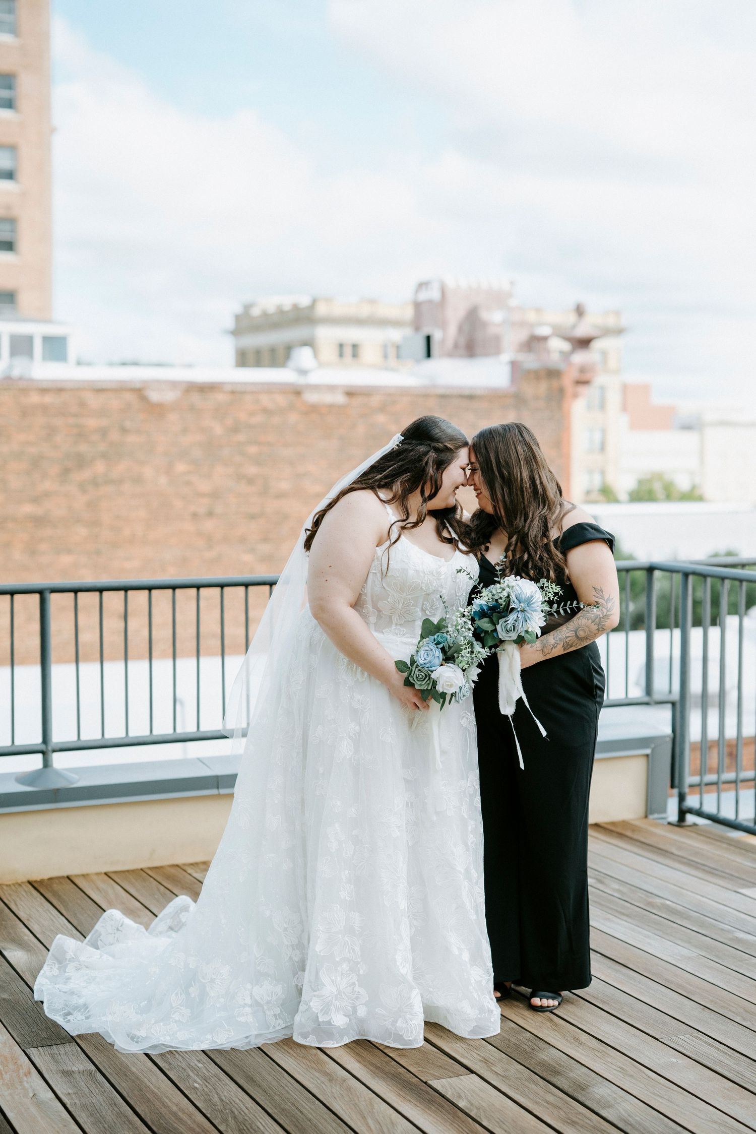 Two people share an intimate moment on a rooftop deck with city buildings visible in the background.