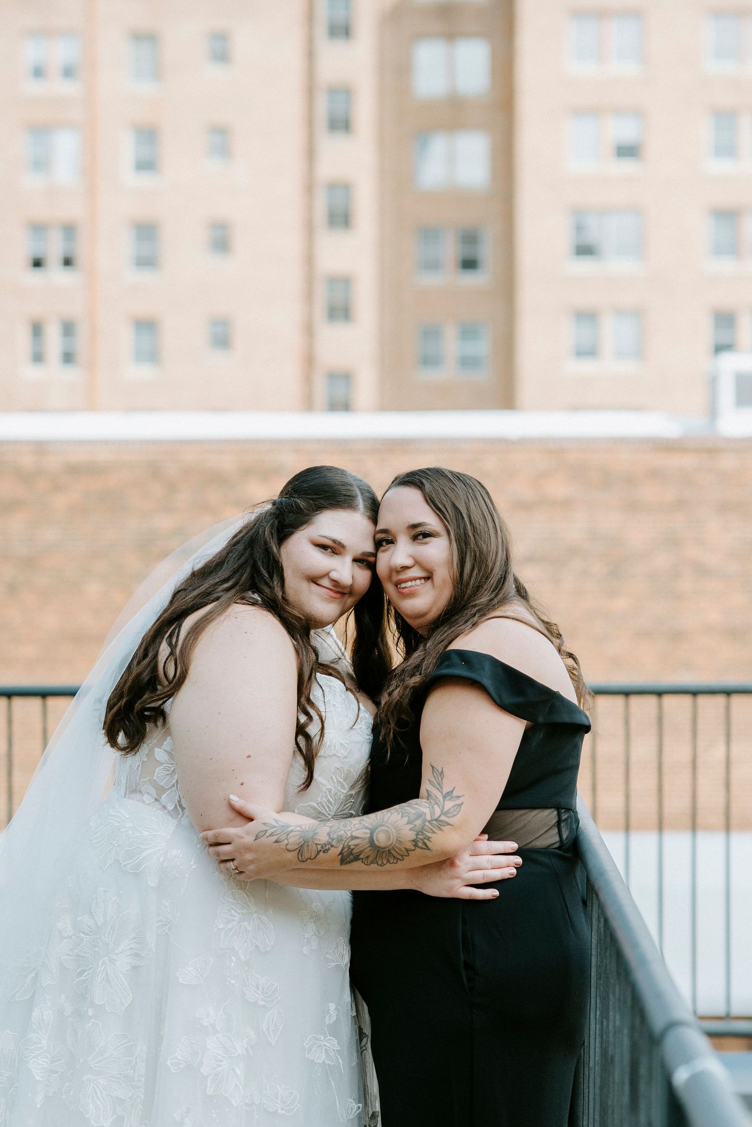 Two people share an intimate moment while embracing on a rooftop with an apartment building in the background.