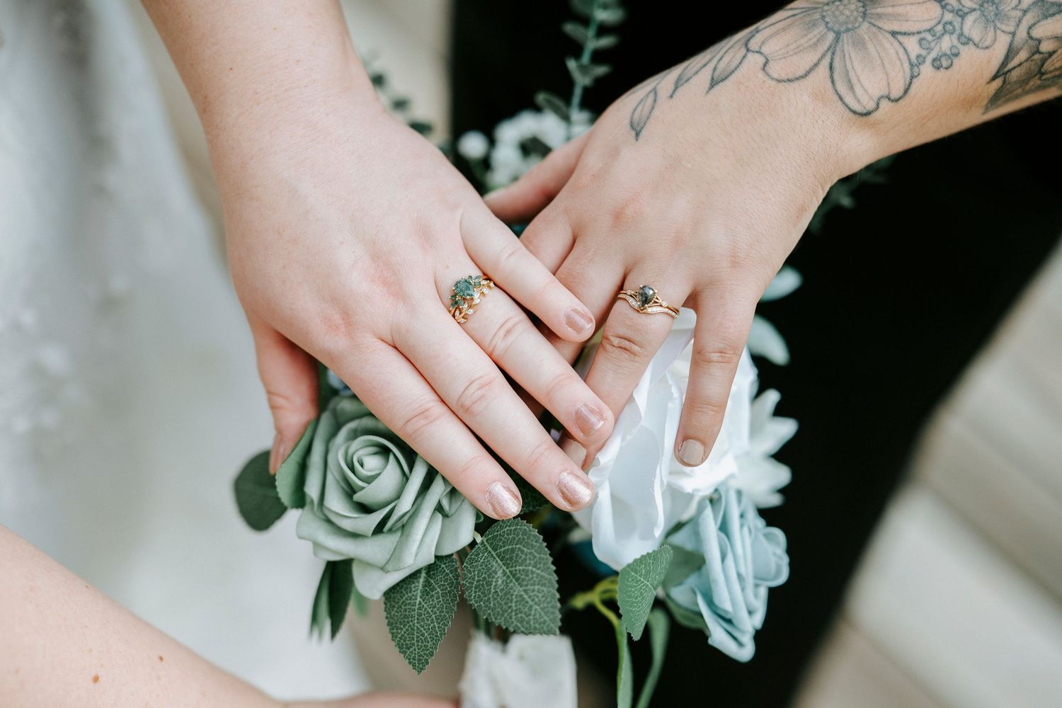 Close-up of hands holding a delicate white and sage green bridal bouquet with eucalyptus leaves and silk ribbons.