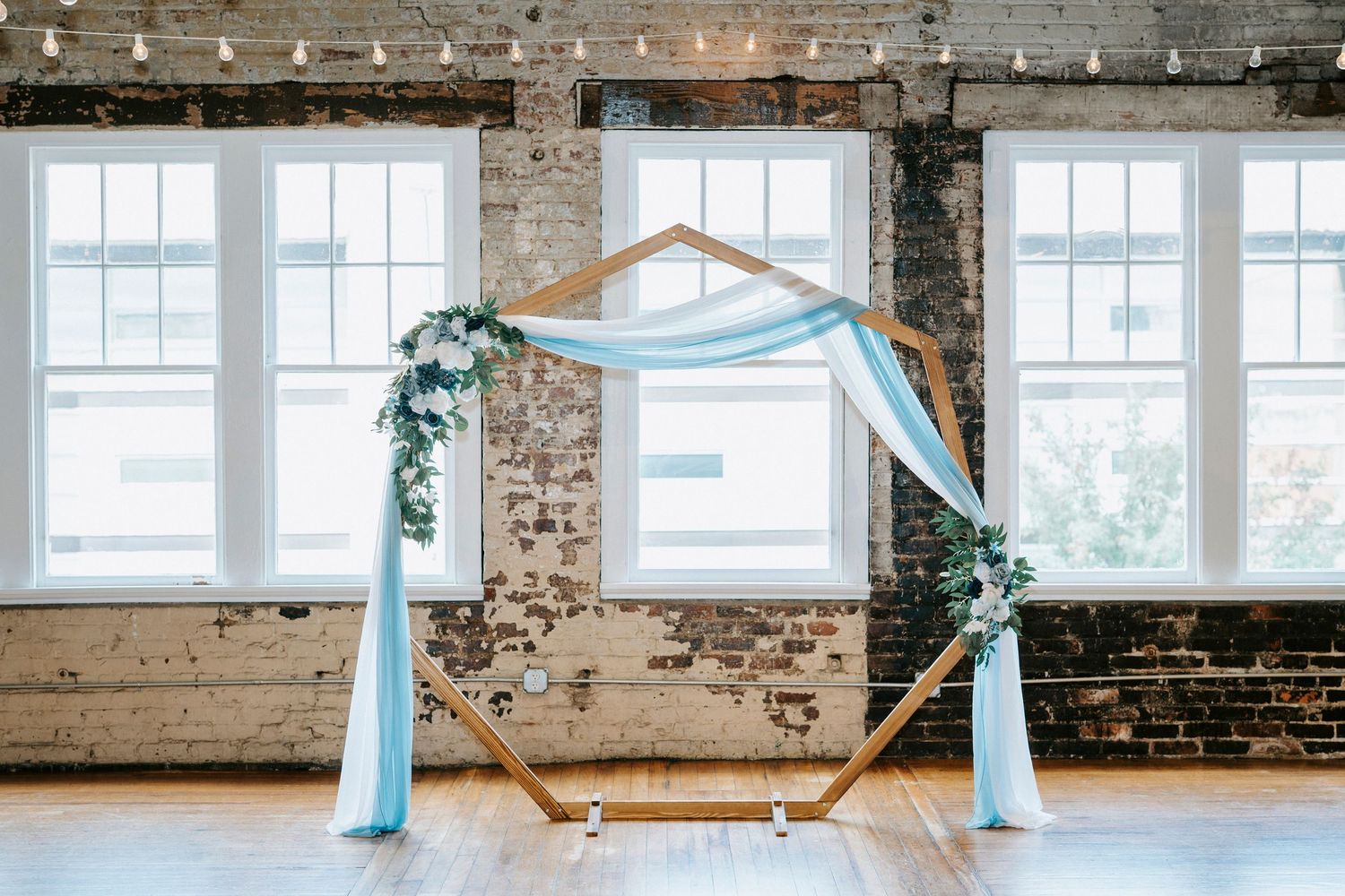 String lights illuminate a rustic industrial venue with exposed brick walls and white-framed windows.