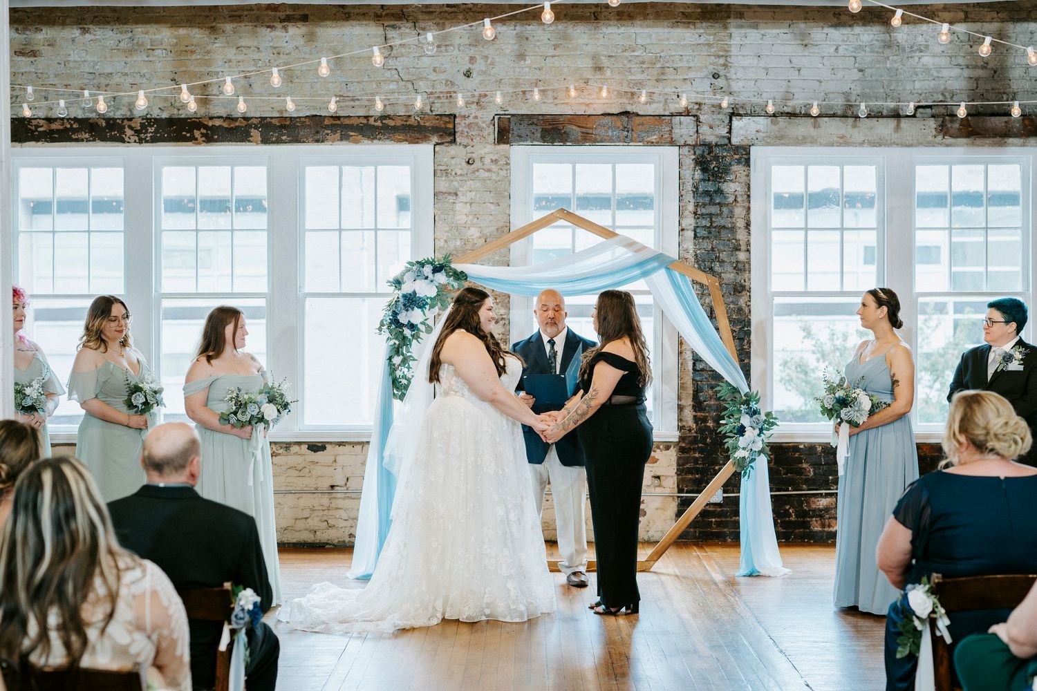 Wedding celebration in an industrial loft space decorated with light blue drapes and string lights.