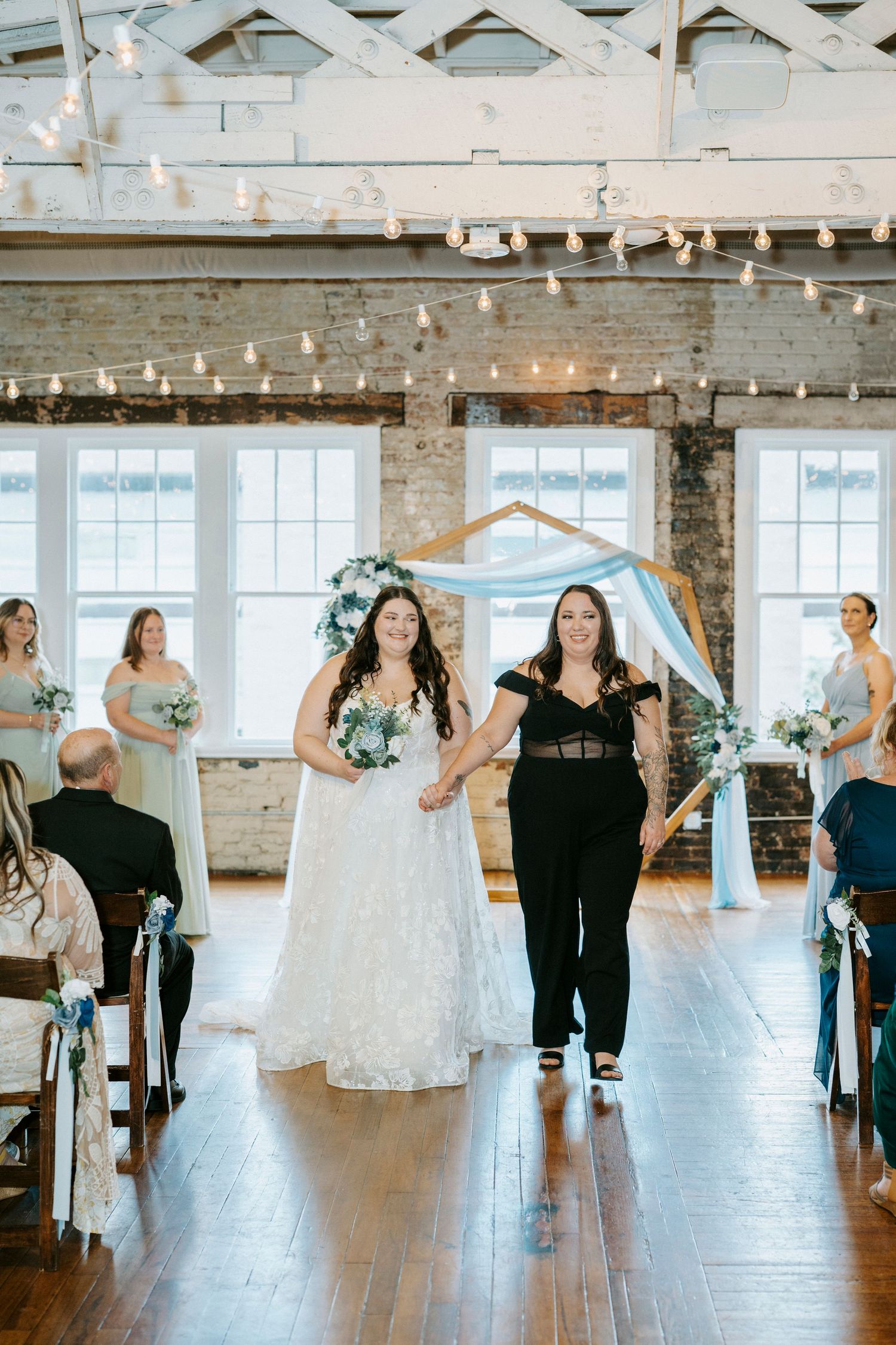 Wedding ceremony in a rustic venue with exposed brick walls, string lights and a hexagonal arch backdrop.