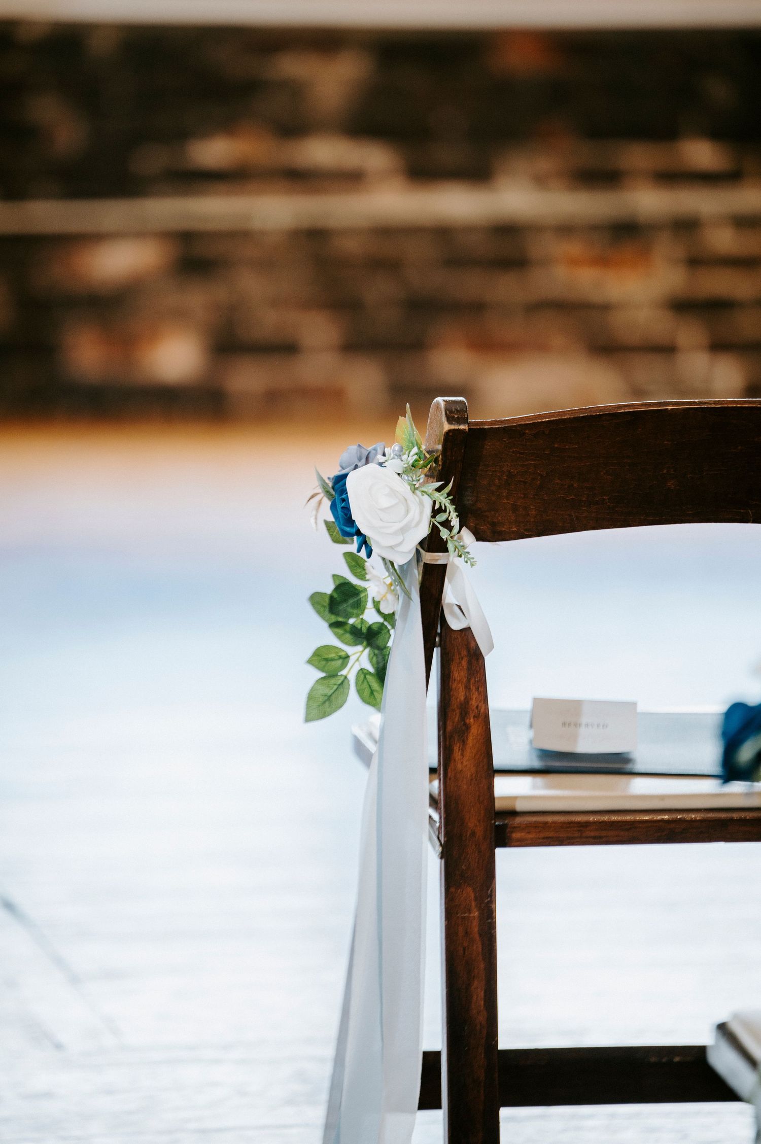 White fabric draped elegantly over dark wooden chairs with delicate green foliage accents for wedding decor.