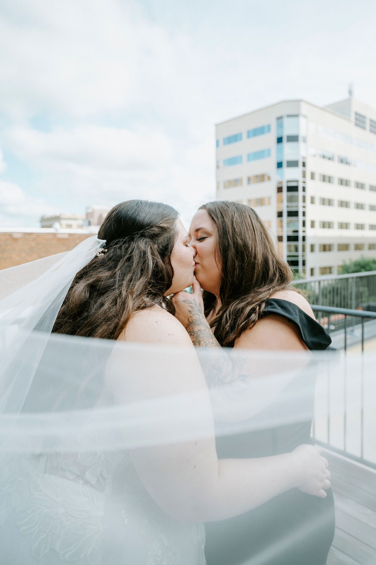 A flowing white veil catches the breeze against a backdrop of modern city buildings.
