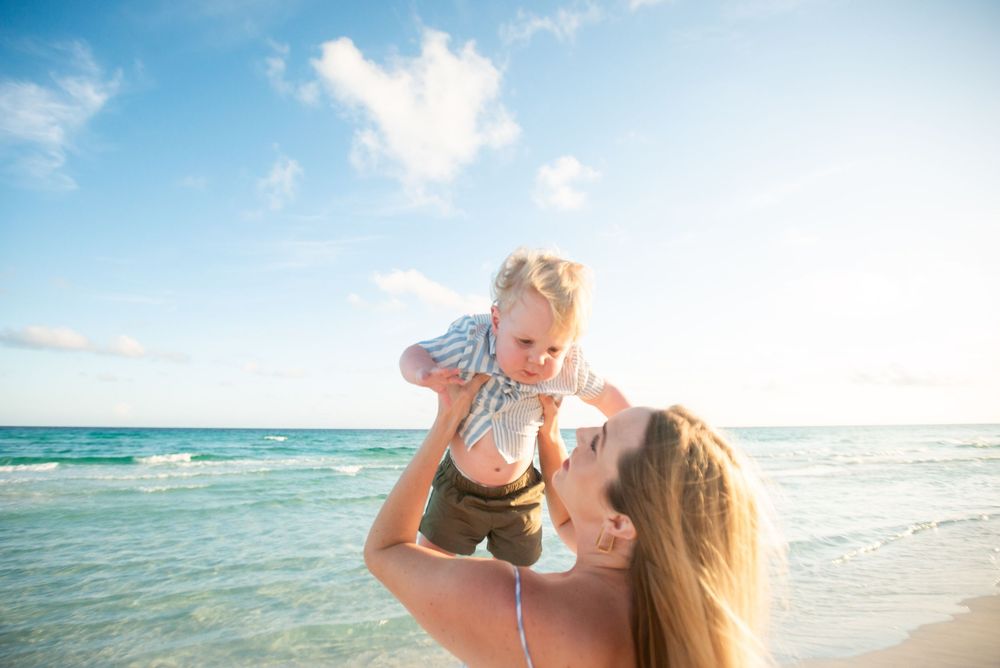 A joyful moment at the beach during sunset as a baby is lifted up against the blue ocean backdrop.