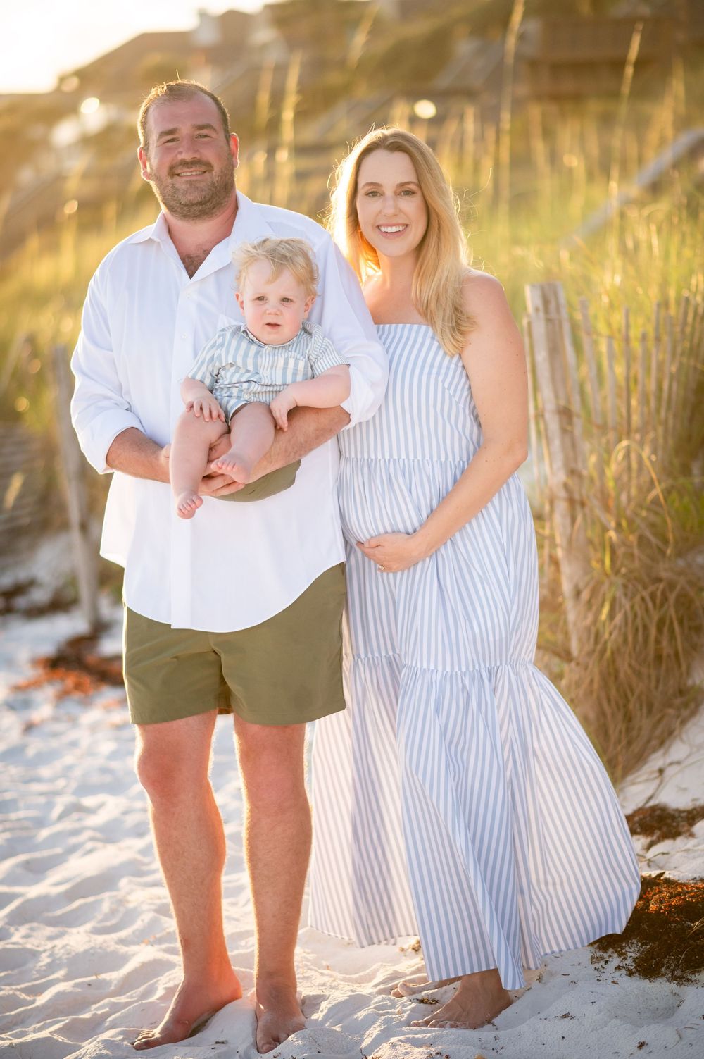 A family poses together on a beach at sunset with tall grass in the background.