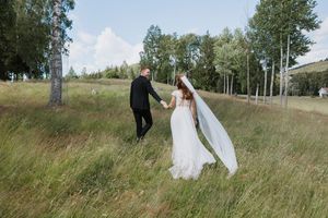 Brudepar som leier hender i en åker. Vinden tar tak i gress og slør.