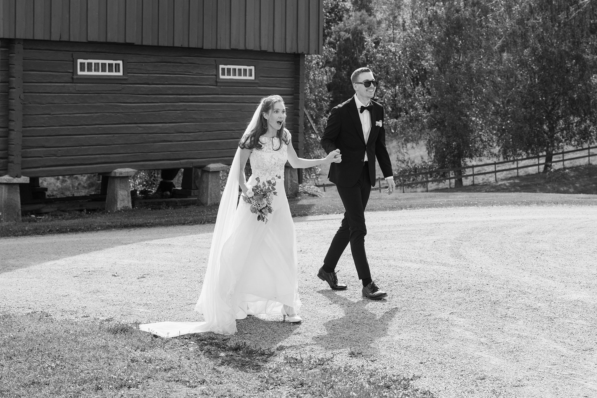 Sort-hvitt bilde av brudepar som går opp til mottagelse til bryllupsgest. Brudgom har på seg solbriller. Bruden ser veldig overasket ut!