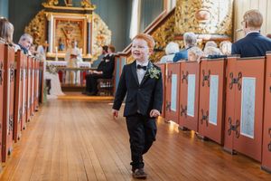 Liten gutt som er pyntet i dress, sløyfe og brystbukett. Han går i midten av kirkegulvet mens alle andre sitter.