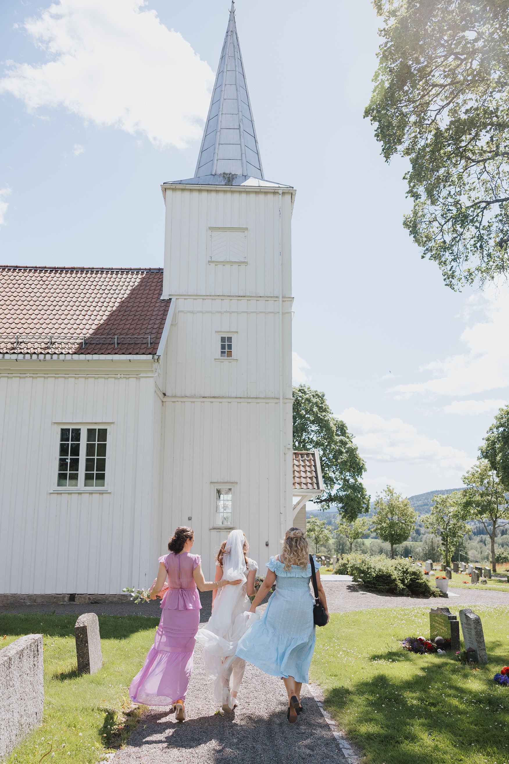 Bruden og forlovere som ankommer kirken. Bak dem ser vi kirken og vinden har tatt tak i både kjoler og slør.