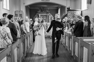 Utmarsj i kirken! Brudeparet holder hender og bærer hvert sitt barn på vei ut. Bruden ser en nær venn og blir veldig rørt.
