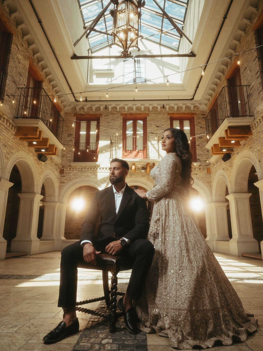 Elegant wedding scene in a grand historic ballroom with ornate architecture and natural light streaming through glass ceiling.