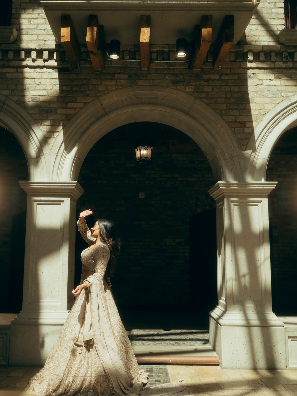 A romantic wedding photoshoot in an elegant arched hallway with dramatic lighting and architectural details.