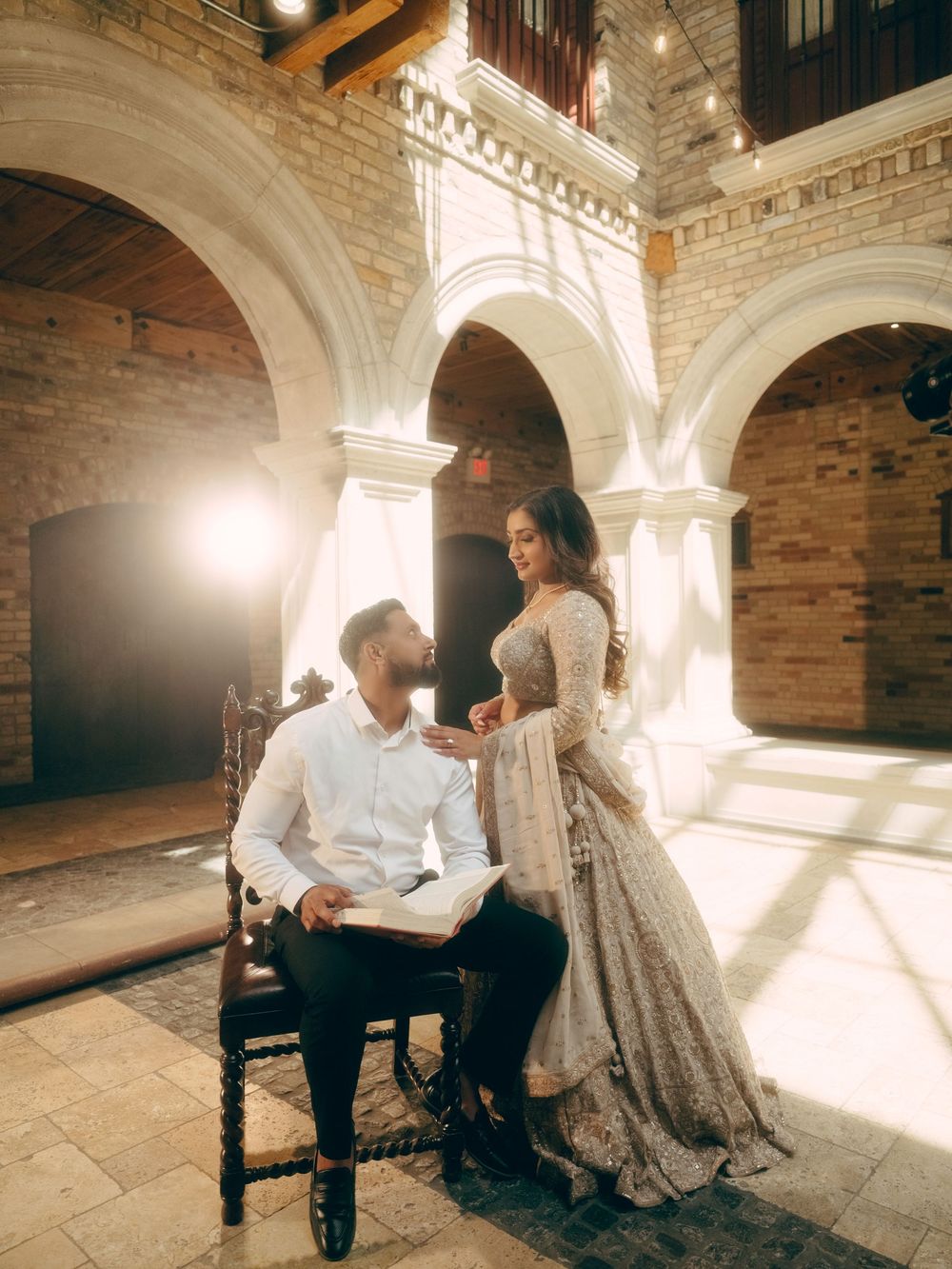Romantic couple in traditional wedding attire share intimate moments in a beautifully lit historic brick archway setting.