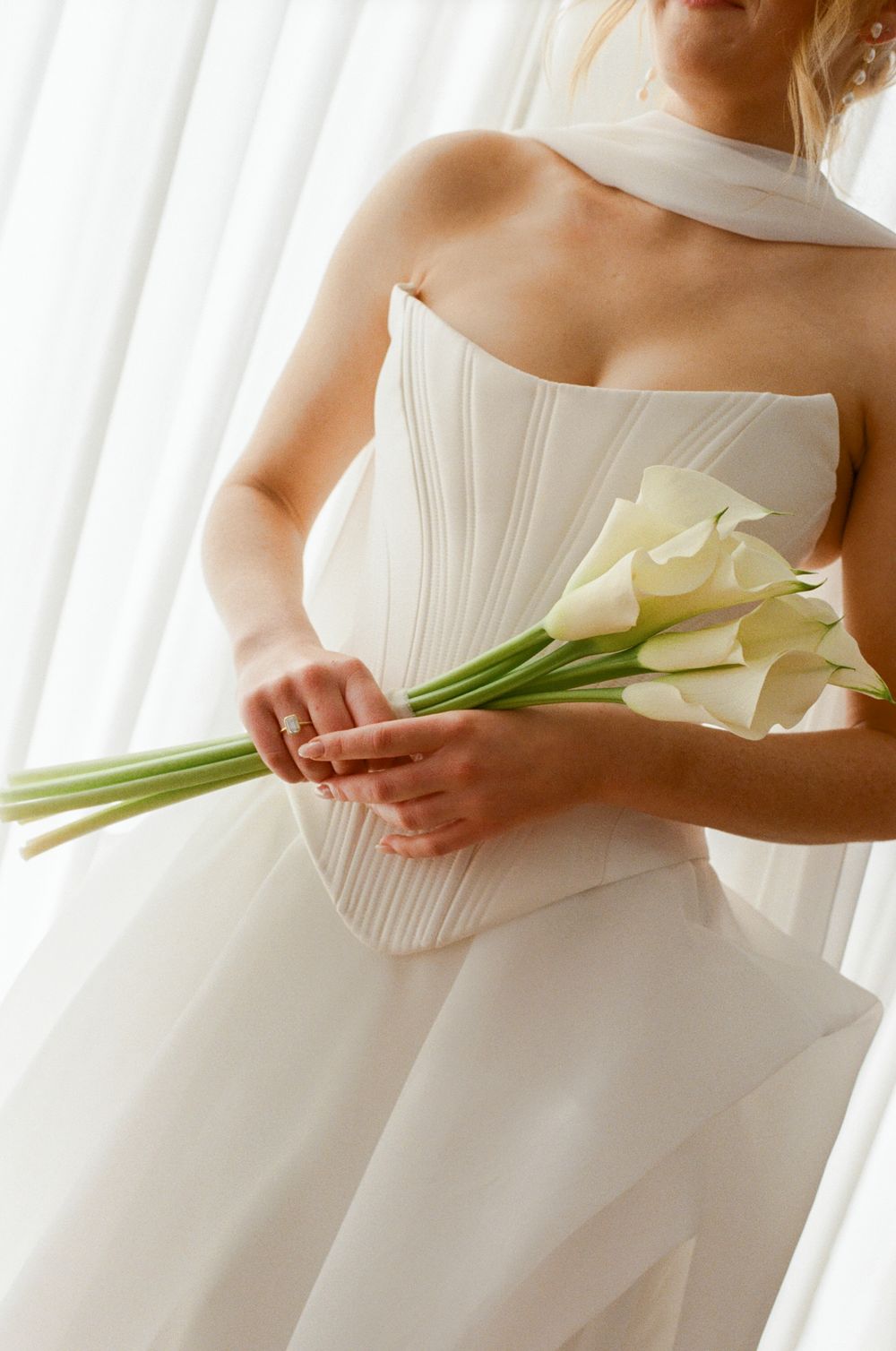 Close-up view of white calla lilies held against a flowing white wedding dress.