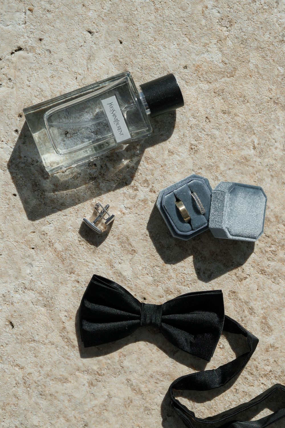 Black bow tie and cologne bottles arranged on textured stone surface.