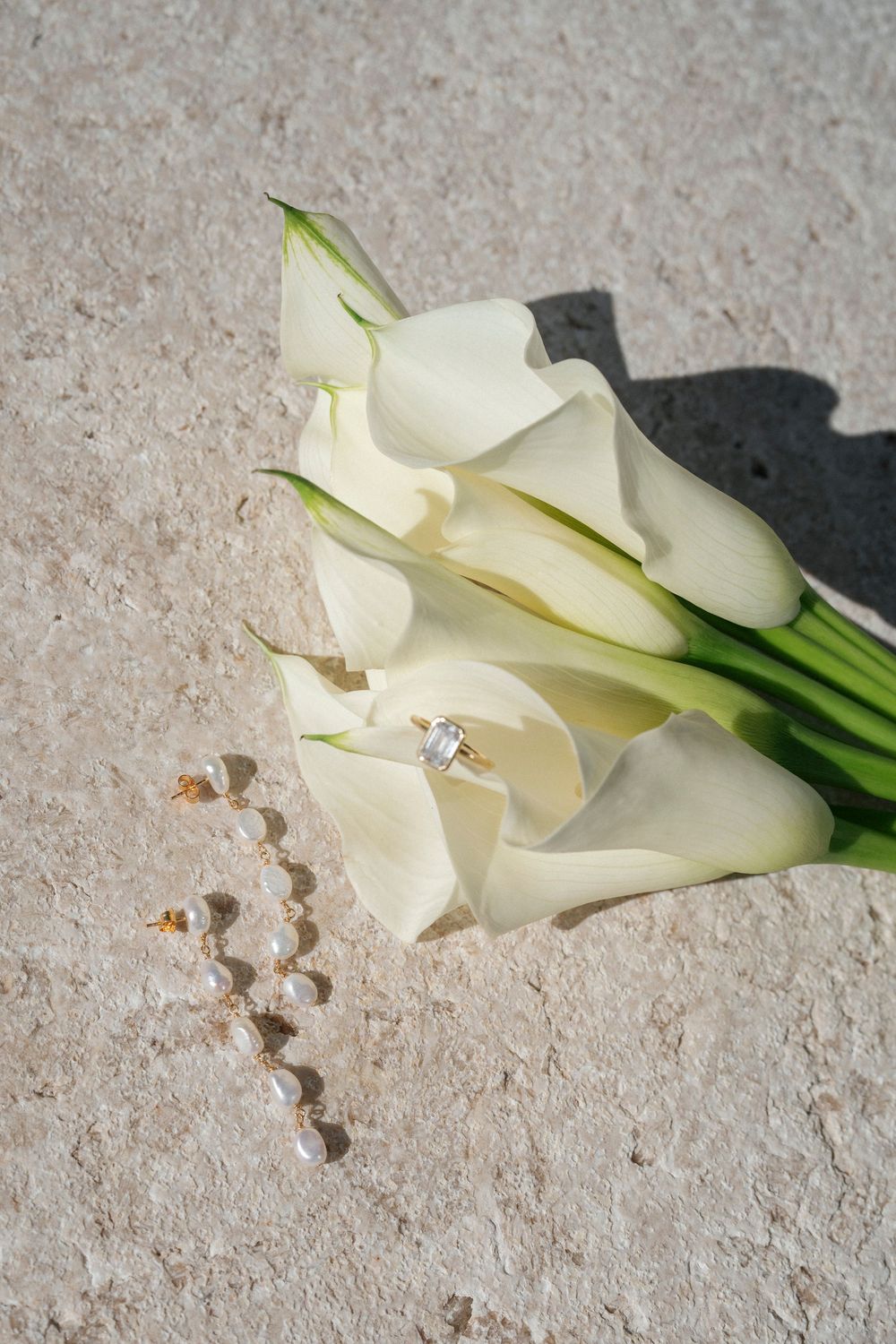 Elegant white calla lilies arranged on textured stone surface.