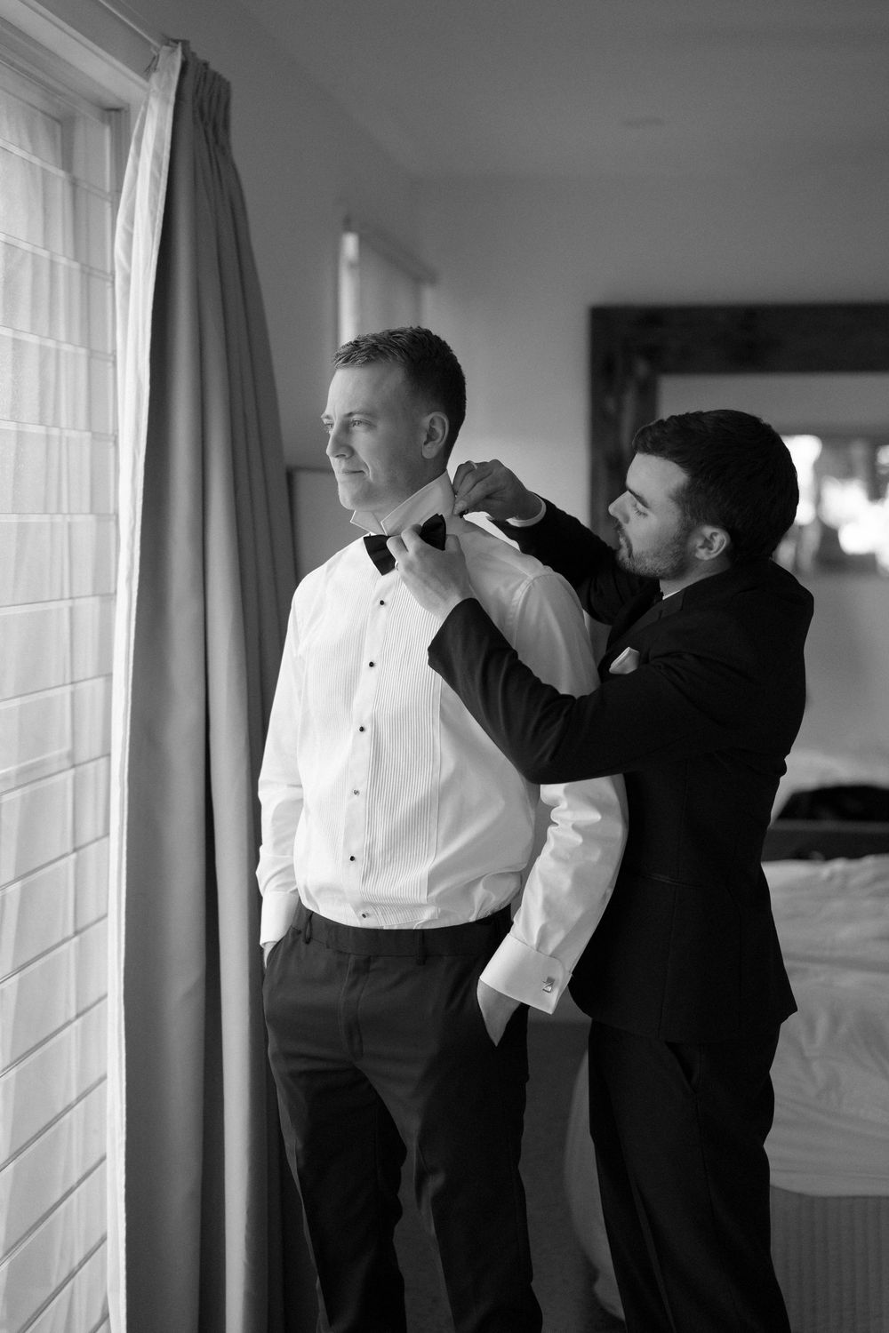 Black and white photo of wedding preparations showing final adjustments being made to formal attire.