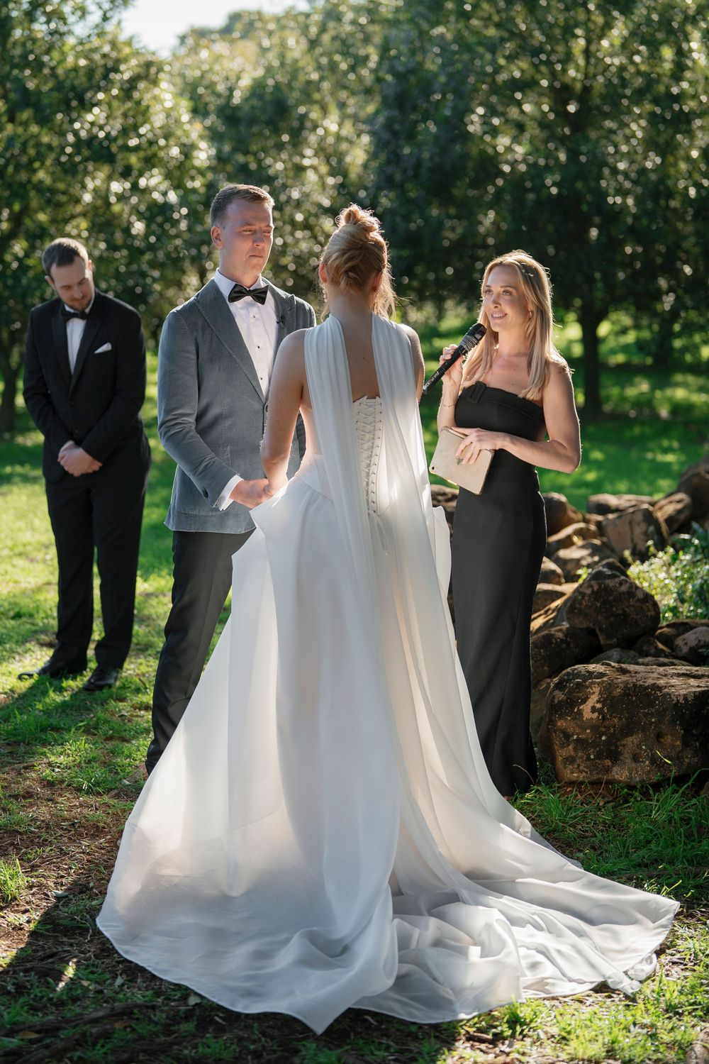 A wedding ceremony takes place in a sunlit garden setting.