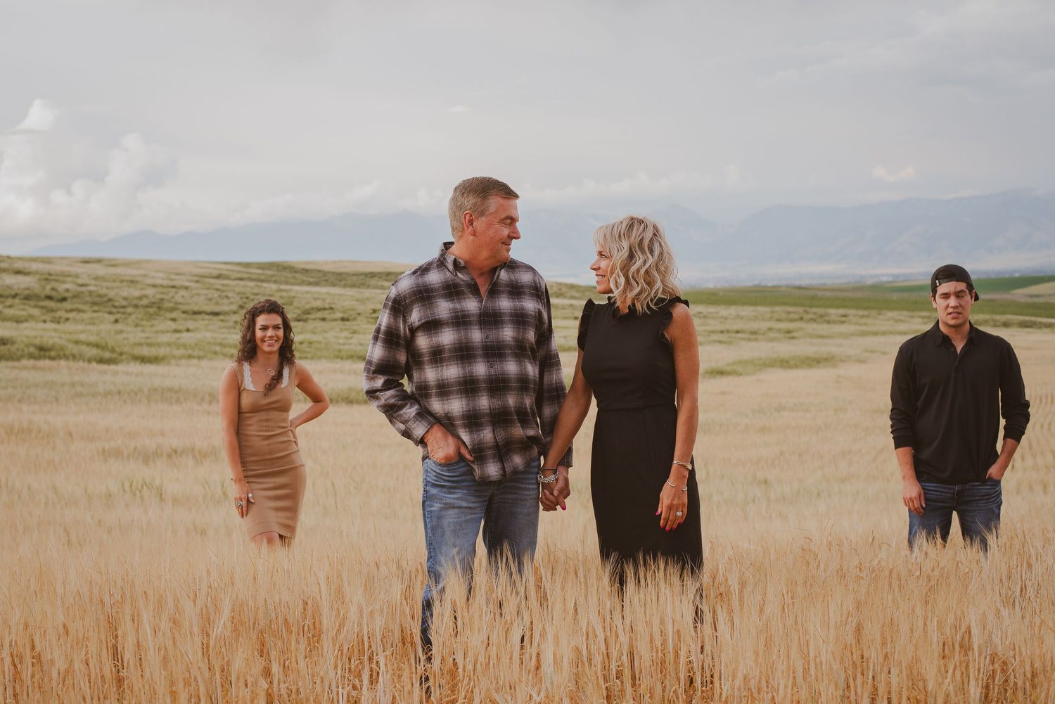 A group walking together through a golden wheat field at sunset with mountains in the distance.