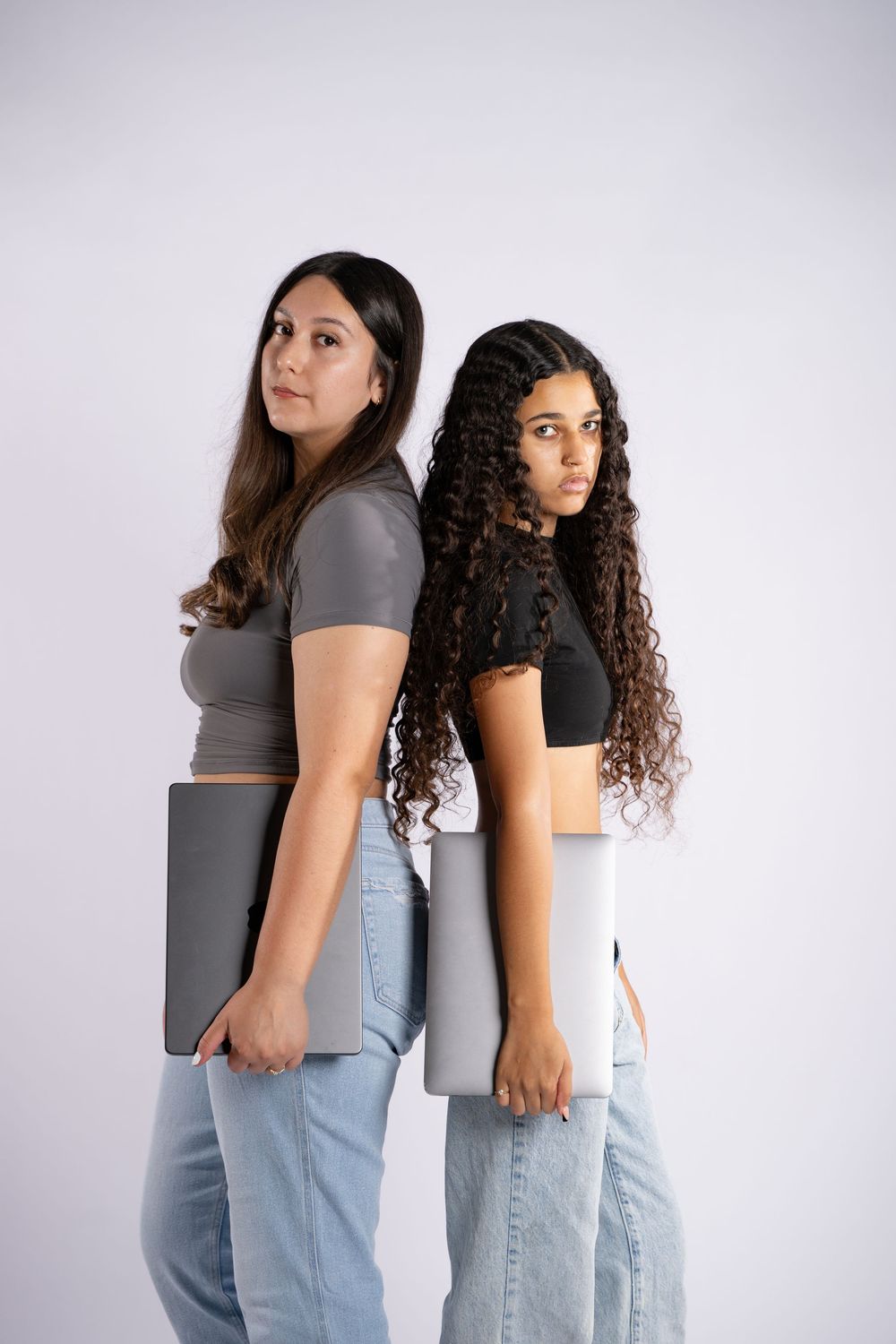 Two photographers stand back-to-back holding laptops in studio setting.